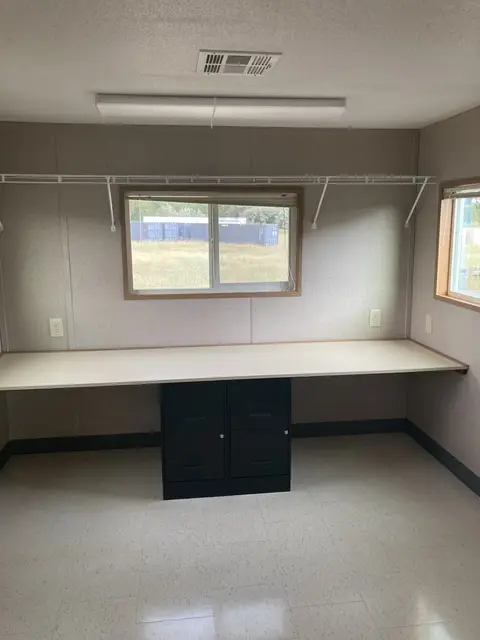 Window-side workstation inside MO-116 with a long desk, filing cabinets, overhead shelving, outlets, and climate control
