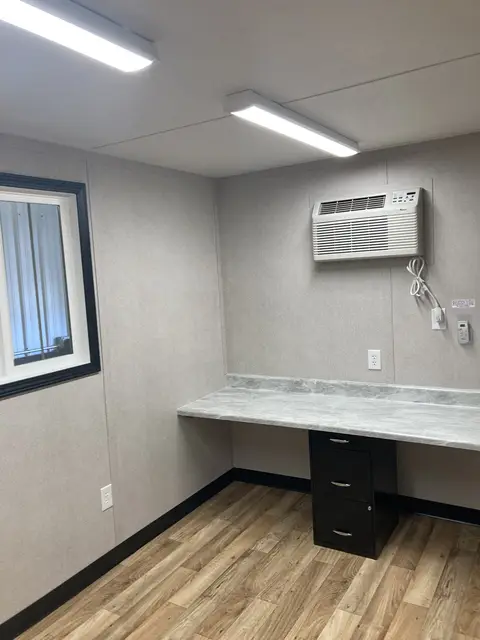 Finished office workstation inside OS-365 with marble-look counter, filing pedestal, window, lighting, outlets, and air conditioner