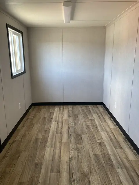 Open finished interior of the O-366 on-ground office with wood-look flooring, window, lighting, and electrical outlets