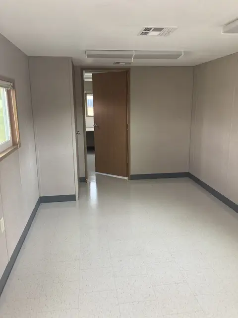 Finished office trailer room with resilient flooring, window, lighting, and interior doorway