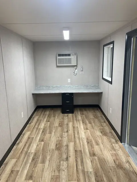Finished container office with wall desk, filing pedestal, air conditioner, and wood-look floor