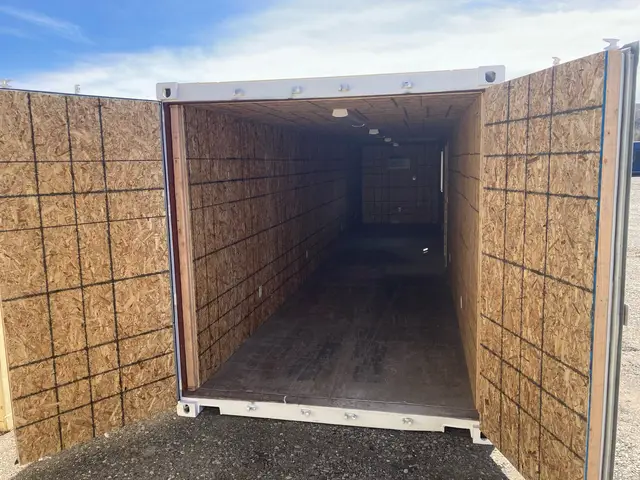 White modified shipping container with open cargo doors and OSB-lined interior