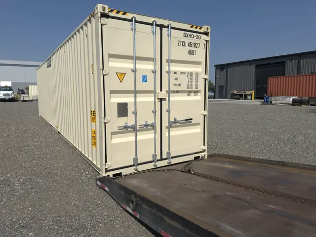 Shipping container aligned with a tilt-bed trailer for loading in the yard