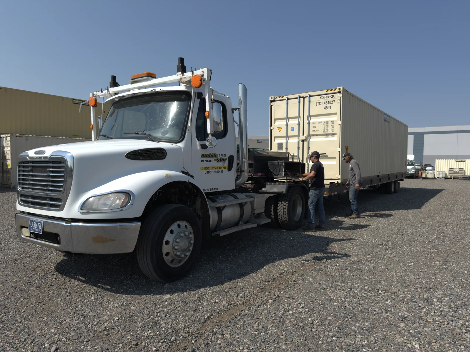 Mobile-Stor crew preparing a shipping container beside the company's tilt-bed delivery truck